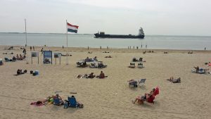 Strand von Vlissingen mit Badegästen und nahem Containerschiff