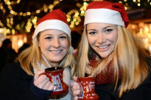 2 Frauen auf Weihnachtsmarkt mit Tassen für Heißgetränke